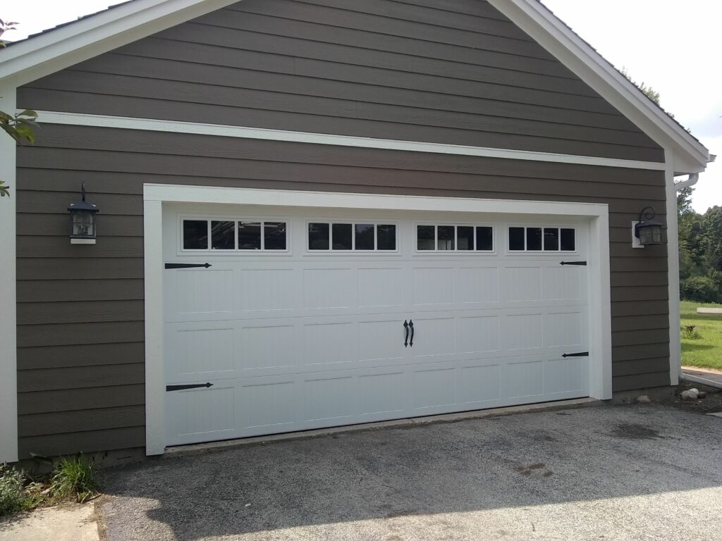 A large white garage door with windows on a brown-sided building, flanked by two black lantern-style lights, under a clear sky.