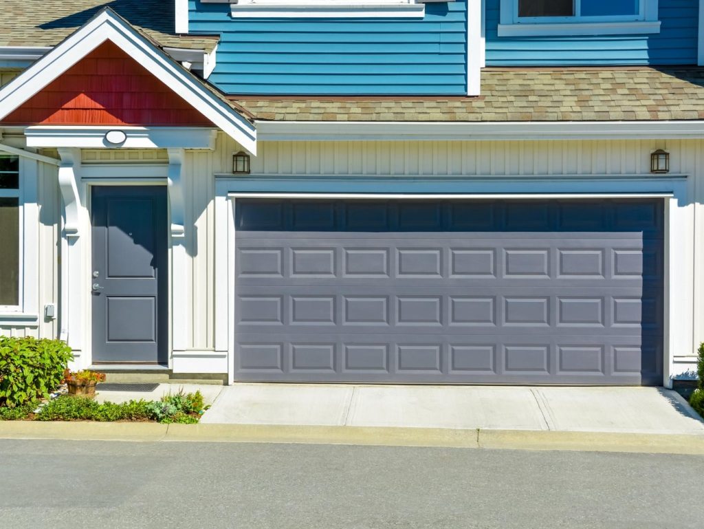 This is an image of a suburban house's facade featuring a closed garage door, a front door with sidelights, and distinct blue siding.