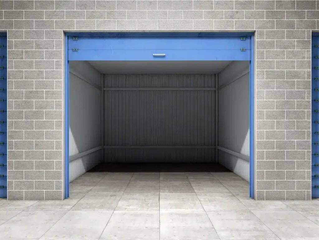 This image shows a storage facility with closed blue roller doors on either side and an open unit in the center revealing an empty space.