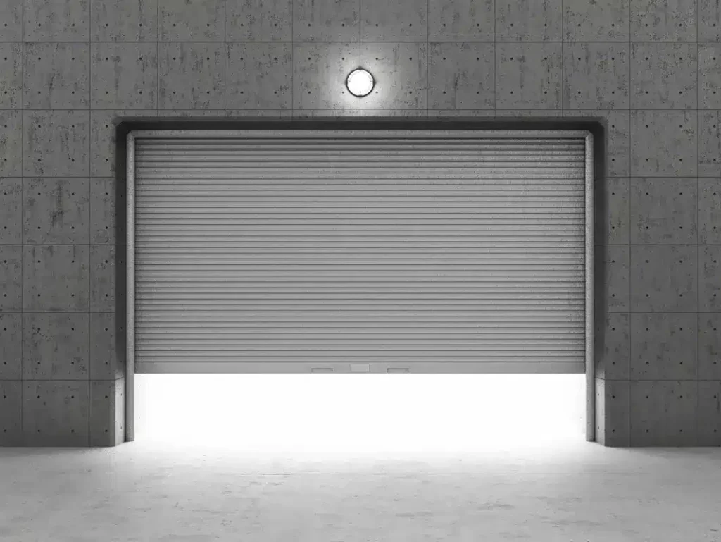 The image depicts a closed rolling shutter door in a minimalist concrete wall with a centrally mounted light above, casting a soft glow on the floor below.